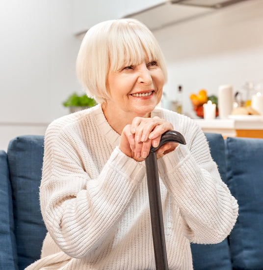 Glad ældre dame med stok sidder i sofaen og smiler