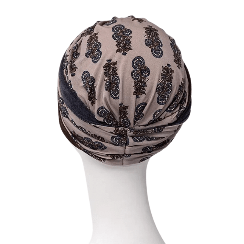 Shakti turban i beige med mørkt paisley-mønster, set bagfra på mannequin med elegant knold i nakken