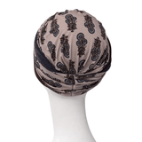 Shakti turban i beige med mørkt paisley-mønster, set bagfra på mannequin med elegant knold i nakken