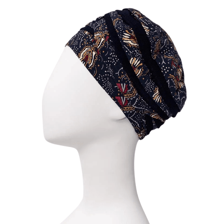 Shanti turban i Amber Garden print set fra siden på en hvid mannequin, med mørkeblå bund og fjer- og stammemotiv